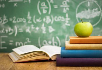 School books with apple on desk School books with apple on desk over green school board background